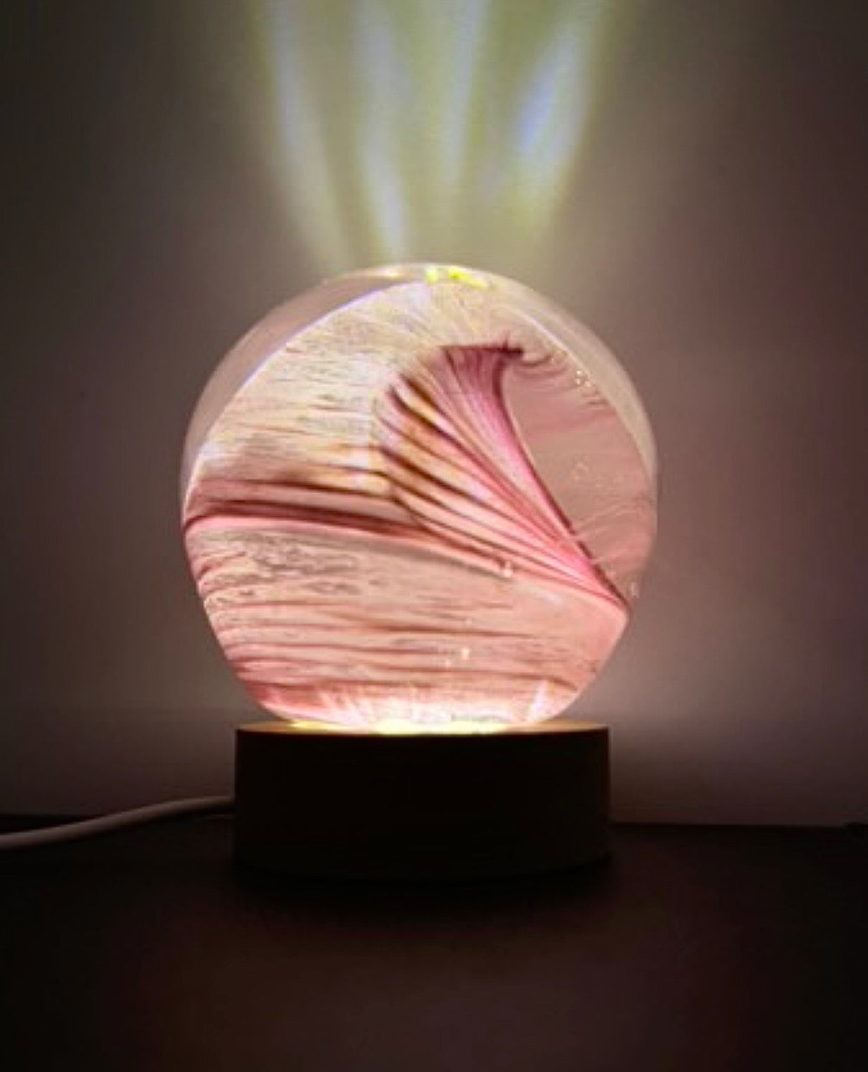 Decorative glass orb with swirling pink wave  patterns on a led ight base. Glass light. Glass orb.