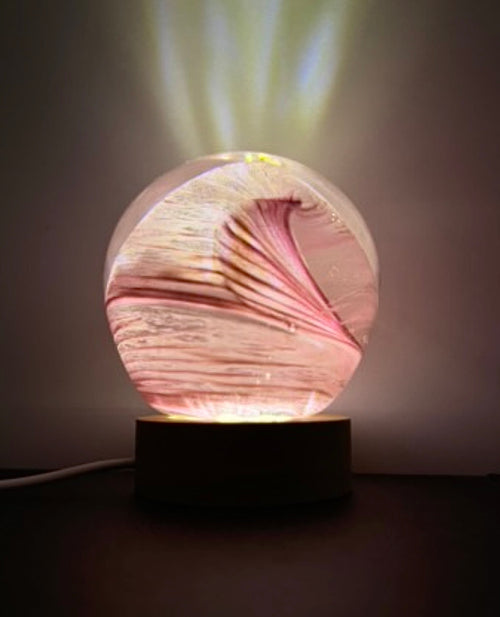 Decorative glass orb with swirling pink wave  patterns on a led ight base. Glass light. Glass orb.